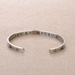 Load image into Gallery viewer, Silver plated bracelet with a message engraved &quot;A mother&#39;s hug lasts long after she lets go&quot; placed on top of a brown fabric
