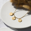 Load image into Gallery viewer, 3 gold disc pendants with engraved initials on gold necklace on grey plate and background with brown pampas decor
