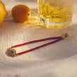 Load image into Gallery viewer, Multicolored Charm Blue Evil Eye Red String bracelet laid out with a bottle in the back
