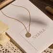 Load image into Gallery viewer, Round LOVE Evil Eye Gold Tone Necklace on top of a SVANA Design card
