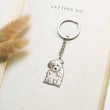 Load image into Gallery viewer, silver dog Personalized Pet Sketch Keychain on a page of an open book 

